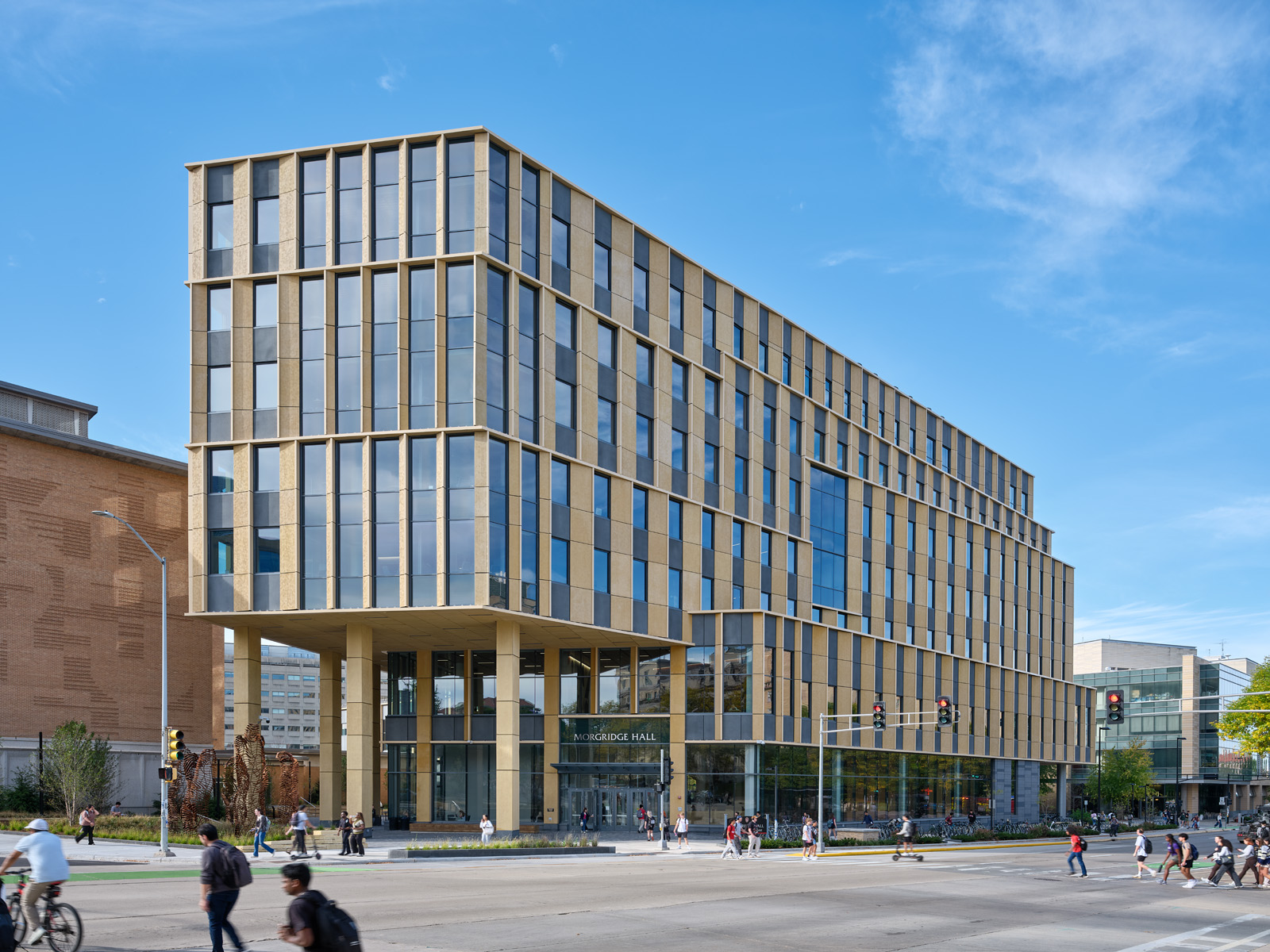 Morgridge Hall with large glass windows and golden vertical panels on a busy city street corner.